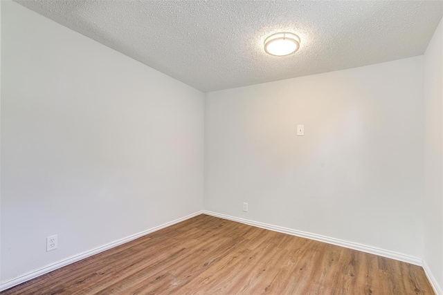 spare room with baseboards, light wood finished floors, and a textured ceiling