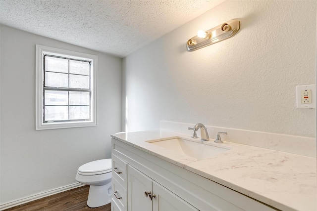 bathroom with vanity, toilet, baseboards, a textured ceiling, and wood finished floors