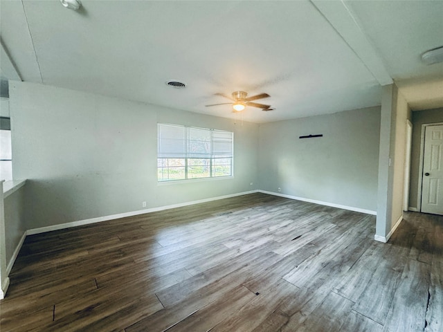 spare room with dark wood-style floors, visible vents, baseboards, and ceiling fan