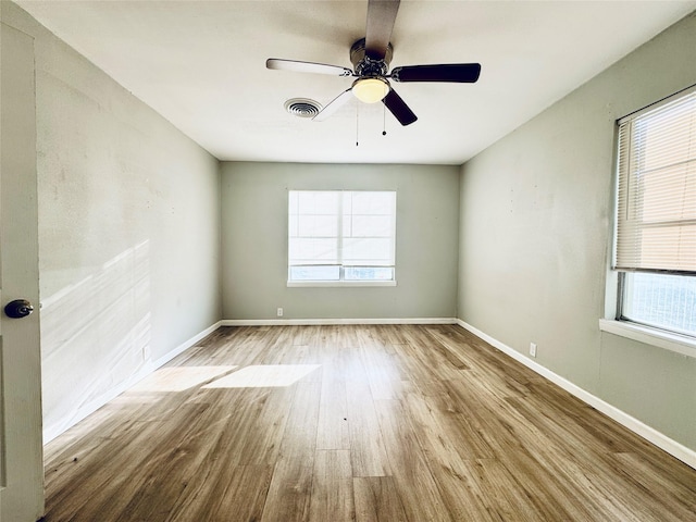 unfurnished room with a wealth of natural light, visible vents, baseboards, and wood finished floors