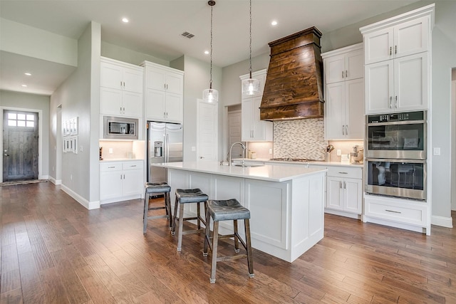 kitchen with light countertops, premium range hood, visible vents, stainless steel appliances, and a sink