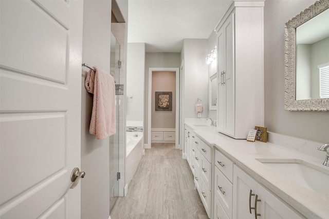 full bath featuring a garden tub, double vanity, a sink, and wood finished floors