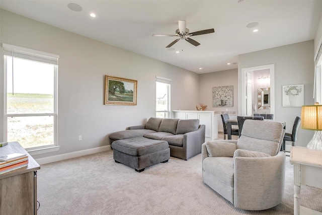 living area with light carpet, ceiling fan, baseboards, and a wealth of natural light
