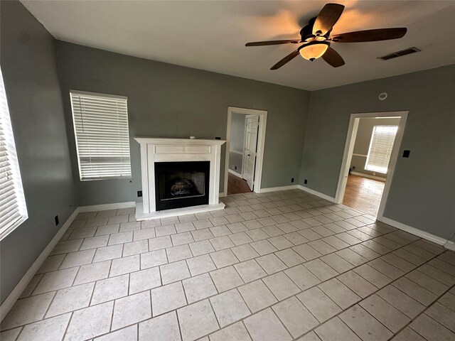 301 E White St, Pilot Point, TX 76258 - unfurnished living room featuring ceiling fan, a fireplace with raised hearth, tile patterned flooring, and baseboards