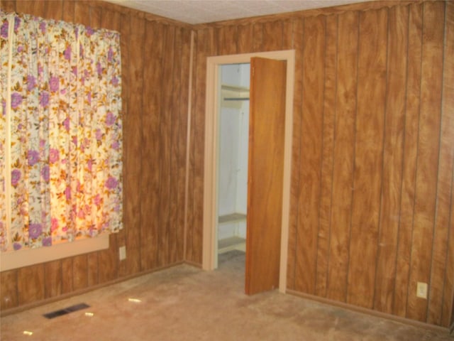 carpeted empty room featuring wood walls and visible vents