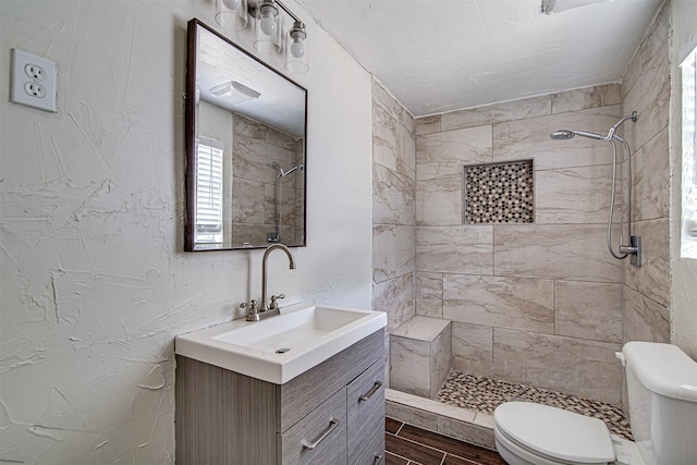 full bathroom featuring vanity, toilet, wood finish floors, a textured wall, and tiled shower