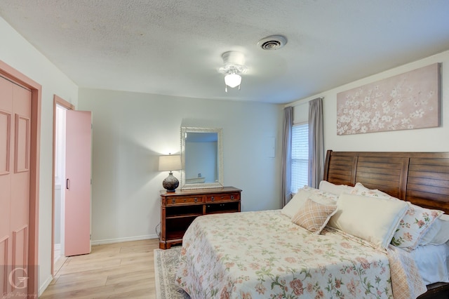 bedroom featuring baseboards, visible vents, light wood-style floors, and a textured ceiling