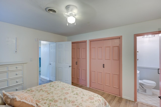 bedroom featuring two closets, ensuite bathroom, light wood-style floors, and visible vents