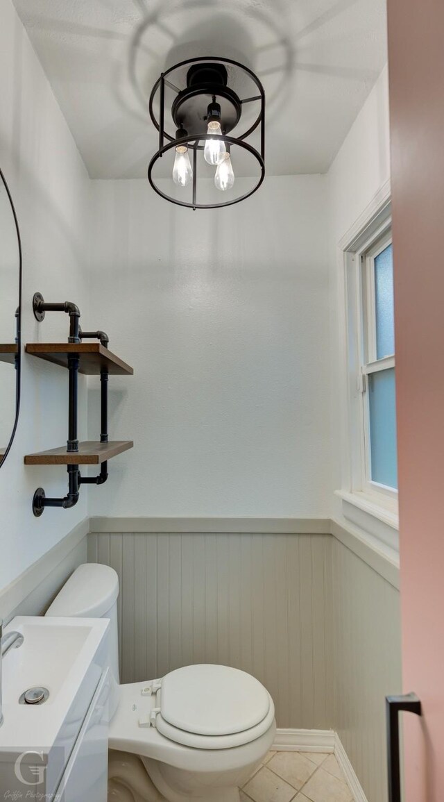half bathroom featuring wainscoting, toilet, tile patterned flooring, and a sink