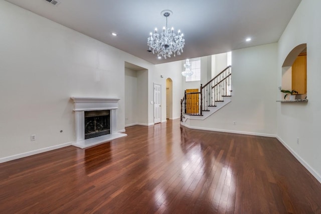 unfurnished living room featuring baseboards, a notable chandelier, arched walkways, and hardwood / wood-style flooring