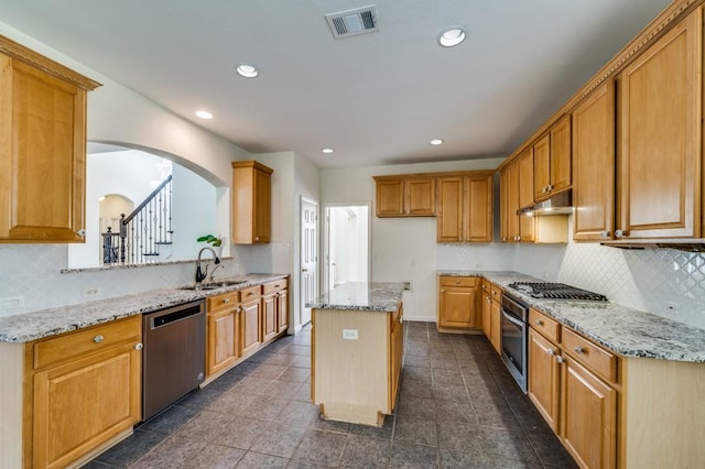 kitchen with under cabinet range hood, a sink, arched walkways, light stone counters, and appliances with stainless steel finishes