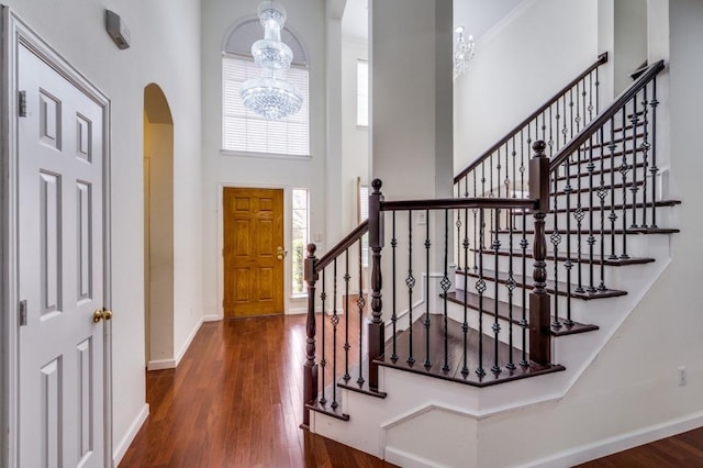 foyer featuring wood finished floors, baseboards, arched walkways, a towering ceiling, and an inviting chandelier