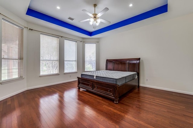 bedroom with hardwood / wood-style floors, visible vents, a tray ceiling, and baseboards