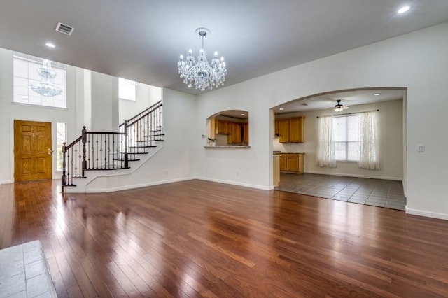 unfurnished living room featuring arched walkways, dark wood-style flooring, visible vents, and stairway