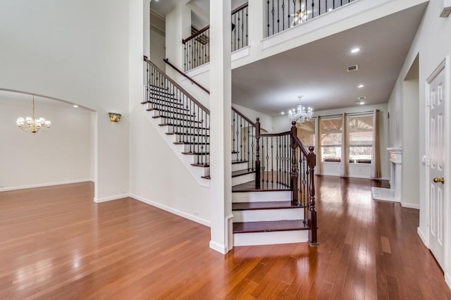 stairway with visible vents, wood finished floors, a towering ceiling, and an inviting chandelier