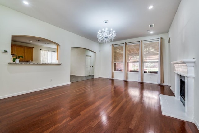 unfurnished living room with plenty of natural light, a fireplace with raised hearth, arched walkways, hardwood / wood-style flooring, and a notable chandelier