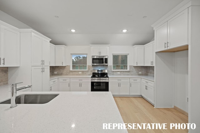 kitchen with a sink, decorative backsplash, appliances with stainless steel finishes, and white cabinetry