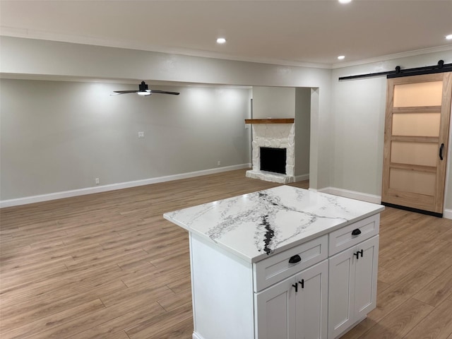 kitchen with a barn door, ceiling fan, light wood-style flooring, ornamental molding, and a kitchen island