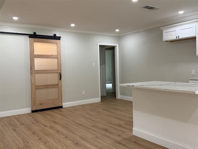 spare room featuring a barn door, light wood-type flooring, and crown molding
