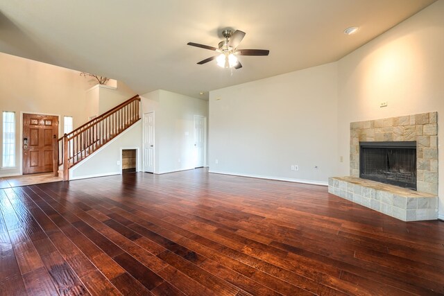 unfurnished living room with hardwood / wood-style flooring, stairs, ceiling fan, a fireplace with raised hearth, and baseboards