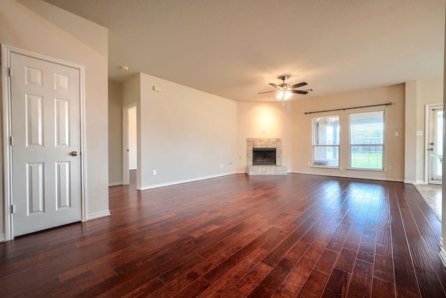 unfurnished living room with a ceiling fan, dark wood-style floors, a fireplace with raised hearth, and baseboards