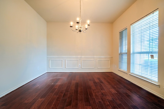 spare room featuring a chandelier, dark wood-type flooring, and wainscoting