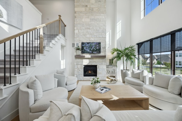 living room featuring stairs, a high ceiling, and a stone fireplace