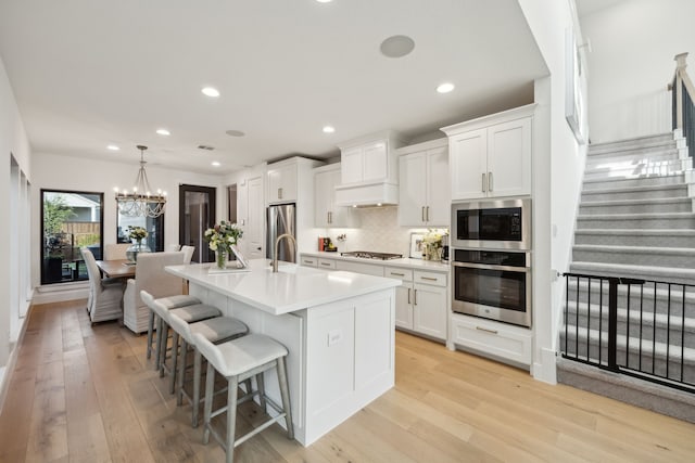 kitchen featuring a notable chandelier, a breakfast bar, a kitchen island with sink, stainless steel appliances, and tasteful backsplash