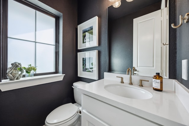 half bath with vanity, a textured wall, and toilet