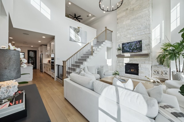 living area with a towering ceiling, a fireplace, a notable chandelier, stairs, and light wood-style flooring