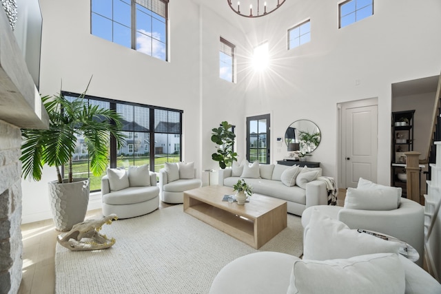 living room with a stone fireplace, a towering ceiling, wood finished floors, and a chandelier