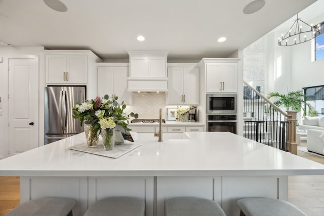 kitchen featuring a kitchen island with sink, a kitchen breakfast bar, white cabinetry, a notable chandelier, and stainless steel appliances