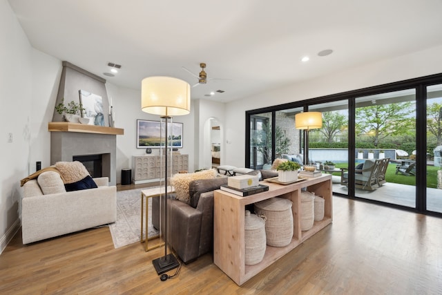 living area featuring a large fireplace, light wood finished floors, arched walkways, and plenty of natural light