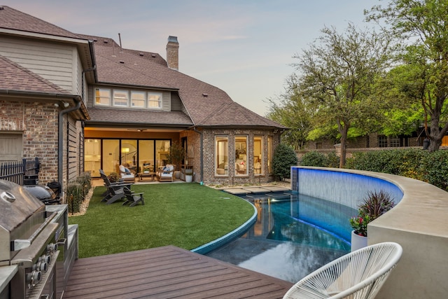 rear view of house with an outdoor living space, a lawn, brick siding, a chimney, and a fenced in pool
