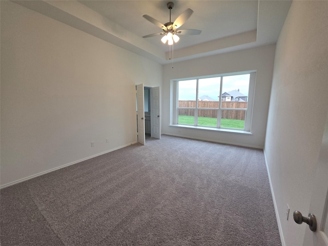 carpeted spare room with baseboards, a raised ceiling, and ceiling fan