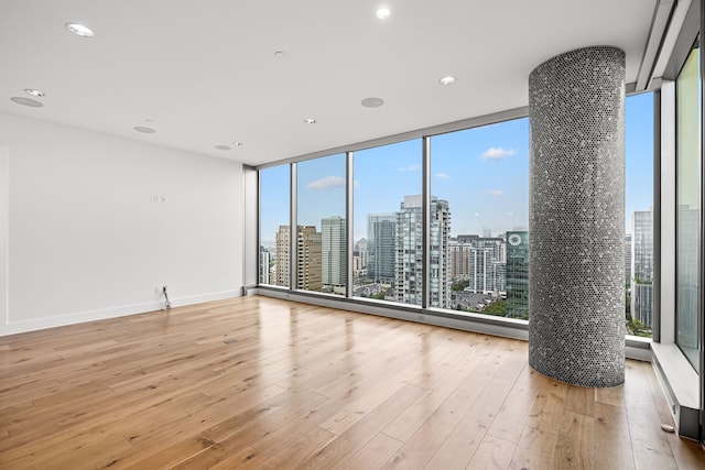 unfurnished room featuring a city view, light wood-style flooring, and a healthy amount of sunlight