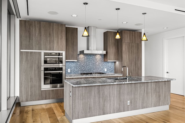 kitchen with wall chimney range hood, gas cooktop, stainless steel double oven, modern cabinets, and a sink