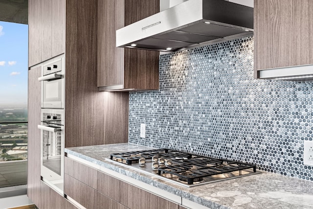 kitchen featuring tasteful backsplash, range hood, modern cabinets, light countertops, and stainless steel appliances