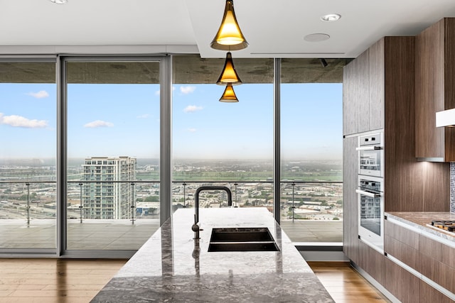 kitchen with stone counters, modern cabinets, a wall of windows, light wood finished floors, and a sink