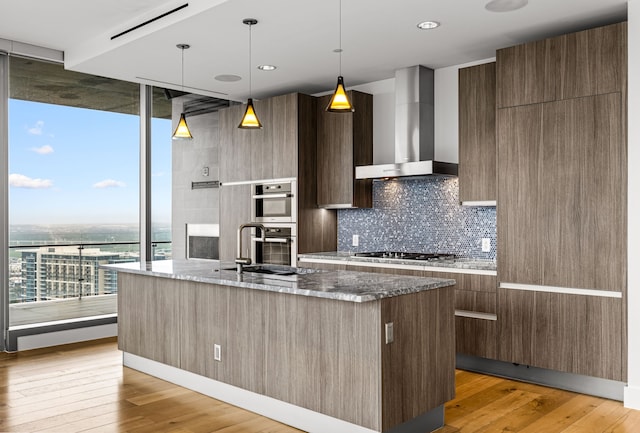 kitchen with modern cabinets, expansive windows, tasteful backsplash, wall chimney range hood, and gas cooktop