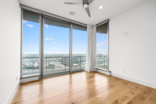 empty room featuring expansive windows, baseboards, a ceiling fan, and wood finished floors