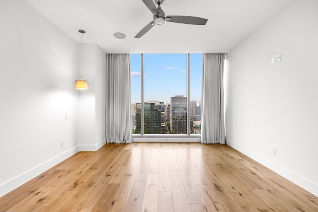empty room featuring wood-type flooring, baseboards, a ceiling fan, and floor to ceiling windows