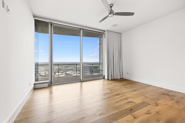 empty room featuring a healthy amount of sunlight, ceiling fan, wood finished floors, and expansive windows
