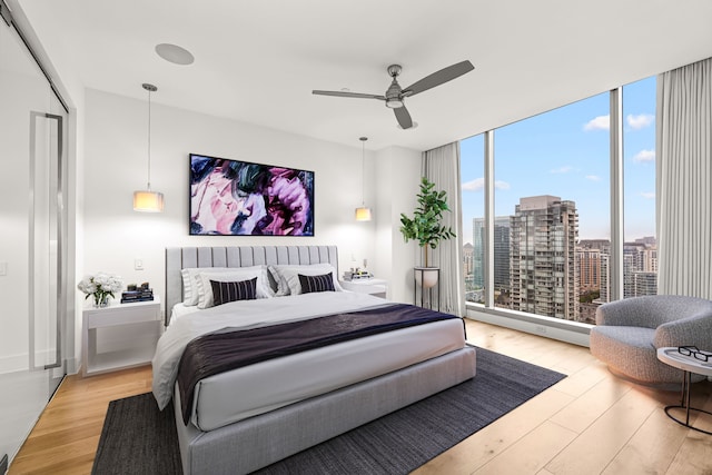bedroom featuring a wall of windows, a ceiling fan, light wood-style floors, and a city view