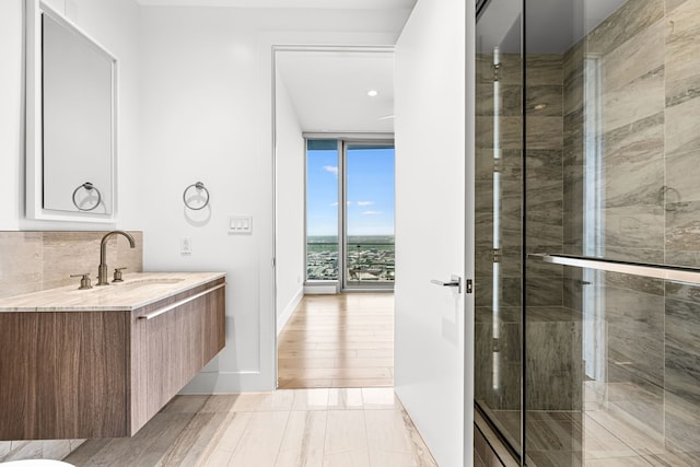 full bathroom featuring vanity, floor to ceiling windows, a stall shower, baseboards, and backsplash