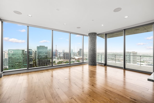 spare room with a wealth of natural light, hardwood / wood-style floors, a view of city, and floor to ceiling windows