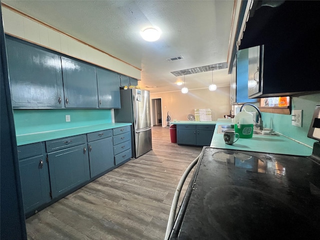 kitchen with freestanding refrigerator, light wood-type flooring, blue cabinetry, visible vents, and a sink