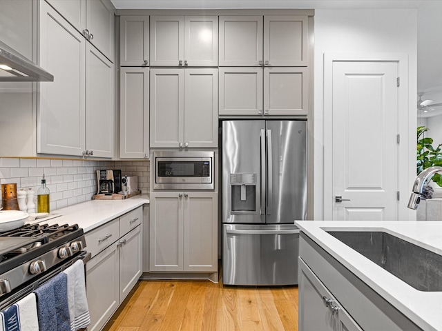 kitchen with stainless steel appliances, gray cabinetry, wall chimney exhaust hood, and a sink