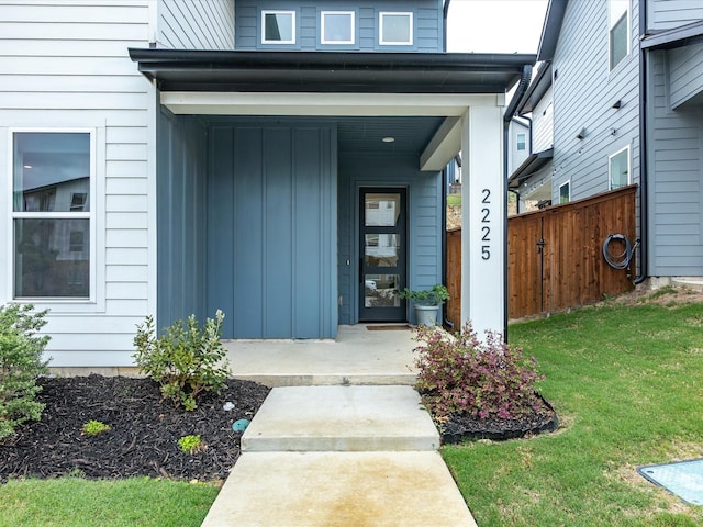entrance to property with board and batten siding, fence, and a yard