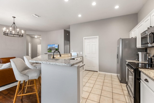 9836 Old Field Dr, Mckinney, TX 75072 - kitchen with a breakfast bar, an inviting chandelier, electric range oven, white cabinetry, and stainless steel microwave